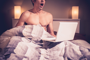 Young man is sitting in bed and watching masturbating laptop